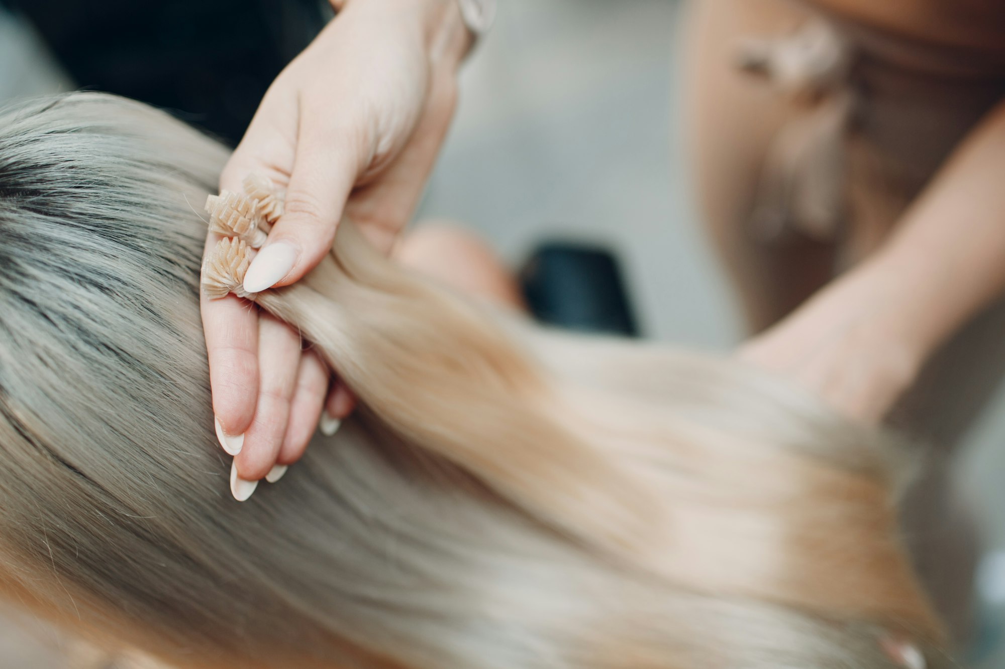 Hairdresser female making hair extensions to young woman with blonde hair in beauty salon.